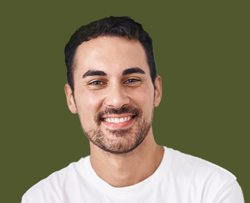 The image shows a smiling man with short hair, wearing a white t-shirt, standing against a green background.